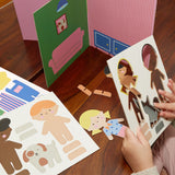 Child’s hands popping out character figures from a cardboard sheet next to a 3D toy house set.