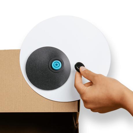 Hand attaching a large googly eye prop onto a cardboard box using a blue plastic connector.