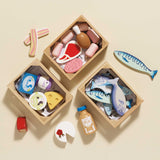 Three wooden crates filled with play food, including fish, meats, and dairy items on a beige surface.