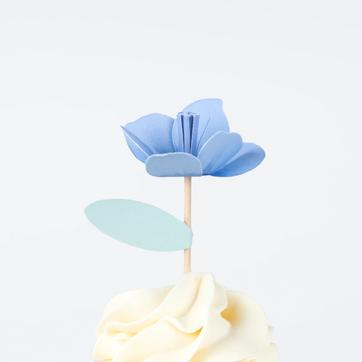 Blue flower cupcake topper with a mint green leaf on a wooden pick, resting on swirled frosting.