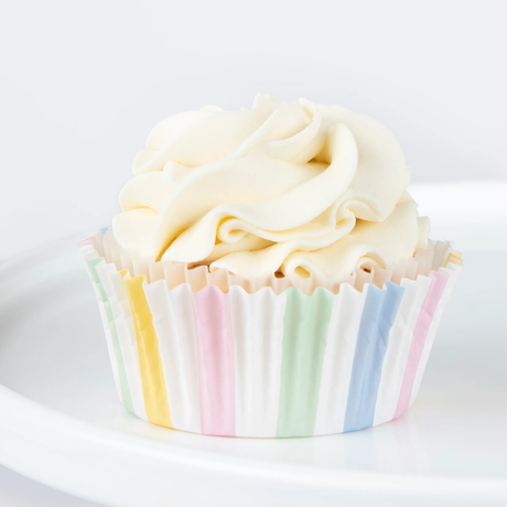 Single cupcake in a pastel striped liner topped with swirled white frosting on a white plate.