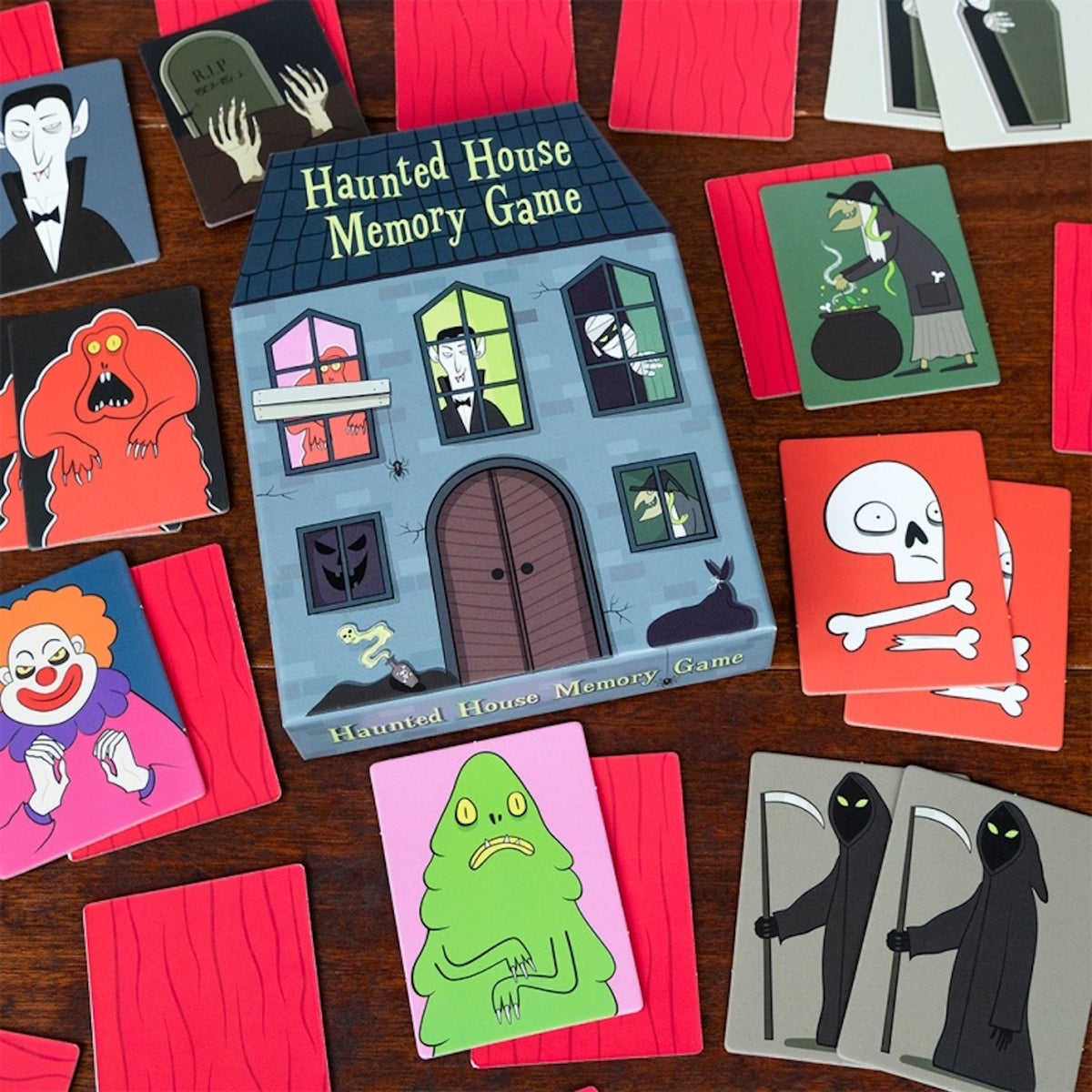 Haunted House Memory Game box surrounded by spooky character matching cards on a wooden background.