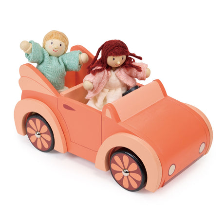 Two wooden dolls riding together inside an orange toy car with flower-patterned wheels.