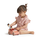 Young girl playing with wooden dolls and an orange toy car.