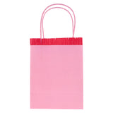 Pink Meri Meri party bag with red fringe detail and pink paper handles, isolated on white background.