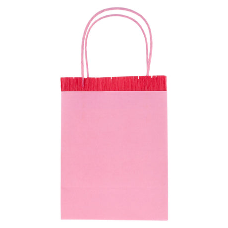 Pink Meri Meri party bag with red fringe detail and pink paper handles, isolated on white background.