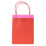 Red paper party gift bag with pink fringed trim and red twine handles on a white background.