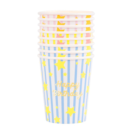 Stacked Meri Meri birthday paper cups with blue, pink, and yellow stripes, gold stars, and "Happy Birthday" text.