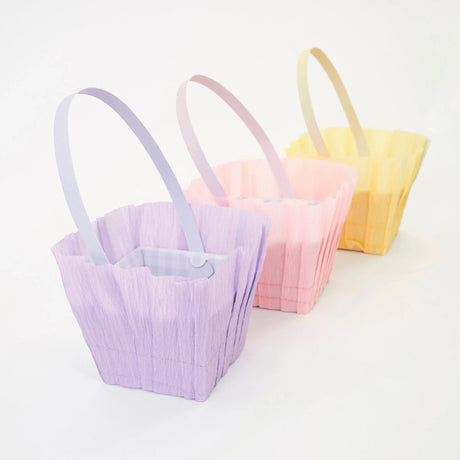 Three pastel crepe paper Easter baskets in purple, pink, and yellow with matching handles for spring celebrations.