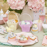 Easter party table with pastel baskets, decorated eggs, cupcakes, and floral hydrangea centerpieces for spring.