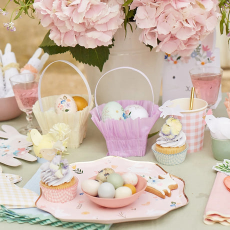 Easter party table with pastel baskets, decorated eggs, cupcakes, and floral hydrangea centerpieces for spring.