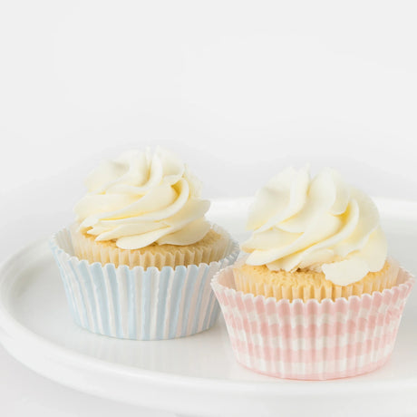 Two vanilla cupcakes with white frosting in blue and pink striped liners on a white plate. Easter cupcake decorating kit.