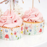 Close-up of two cupcakes with pink piped frosting, fairy-themed floral liners, and toppers on a white surface.