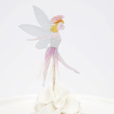 Fairy cupcake topper with wings, a pink tassel skirt, and blonde hair, standing on white frosting.