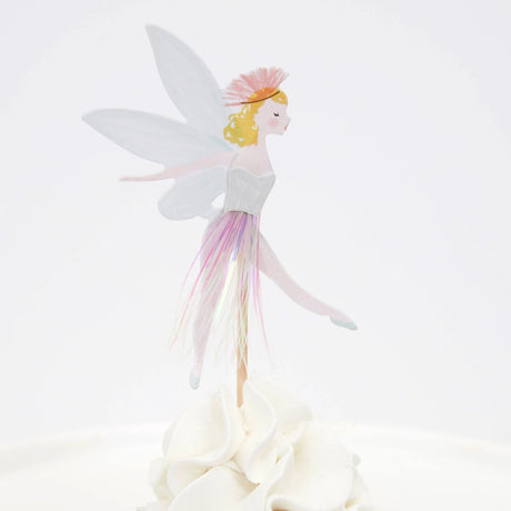 Fairy cupcake topper with wings, a pink tassel skirt, and blonde hair, standing on white frosting.