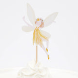 Fairy cupcake topper with white wings, a yellow dress, and a flower crown, placed in white frosting.