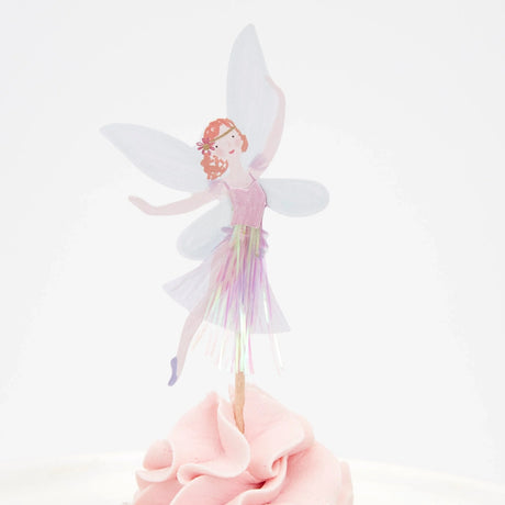 A fairy cupcake topper with translucent wings and a tinsel skirt inserted into pink frosting.