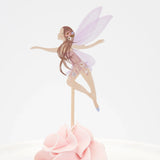 A fairy cupcake topper with purple wings and long brown hair inserted into pink frosting.