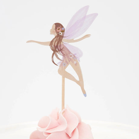A fairy cupcake topper with purple wings and long brown hair inserted into pink frosting.