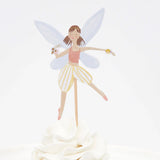 A fairy cupcake topper with wings, a pink top, and striped shorts, stuck into white frosting.