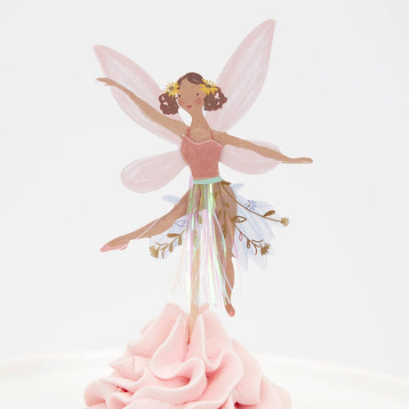A fairy cupcake topper with pink wings and a tinsel skirt, placed in pink frosting.
