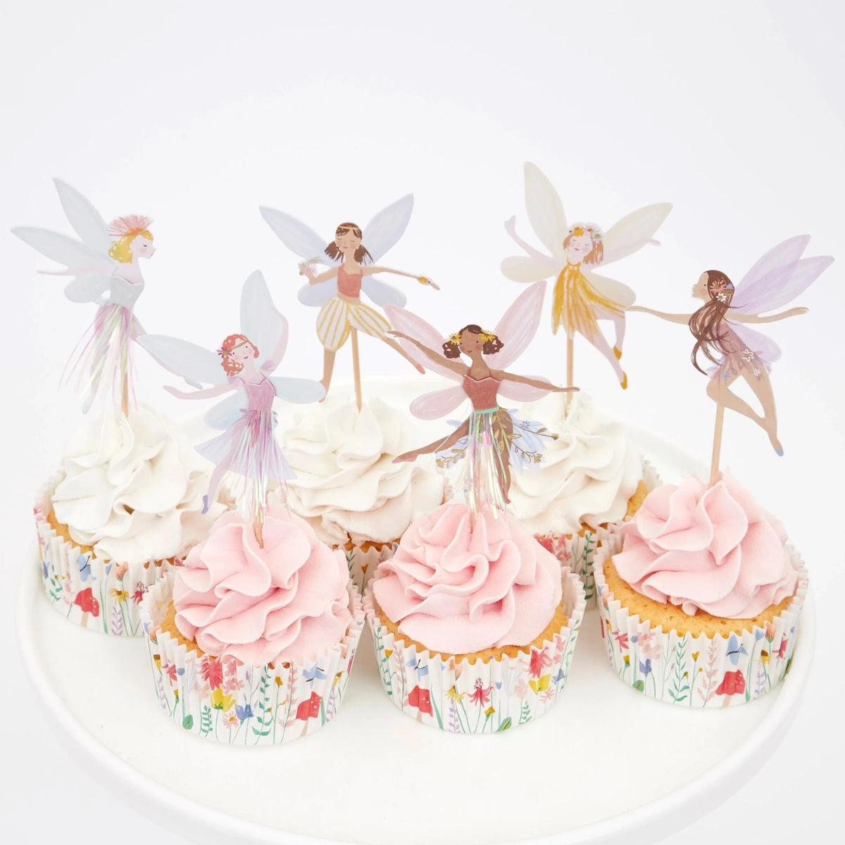 Six cupcakes with pink and white frosting, floral liners, and fairy toppers on a white cake stand.