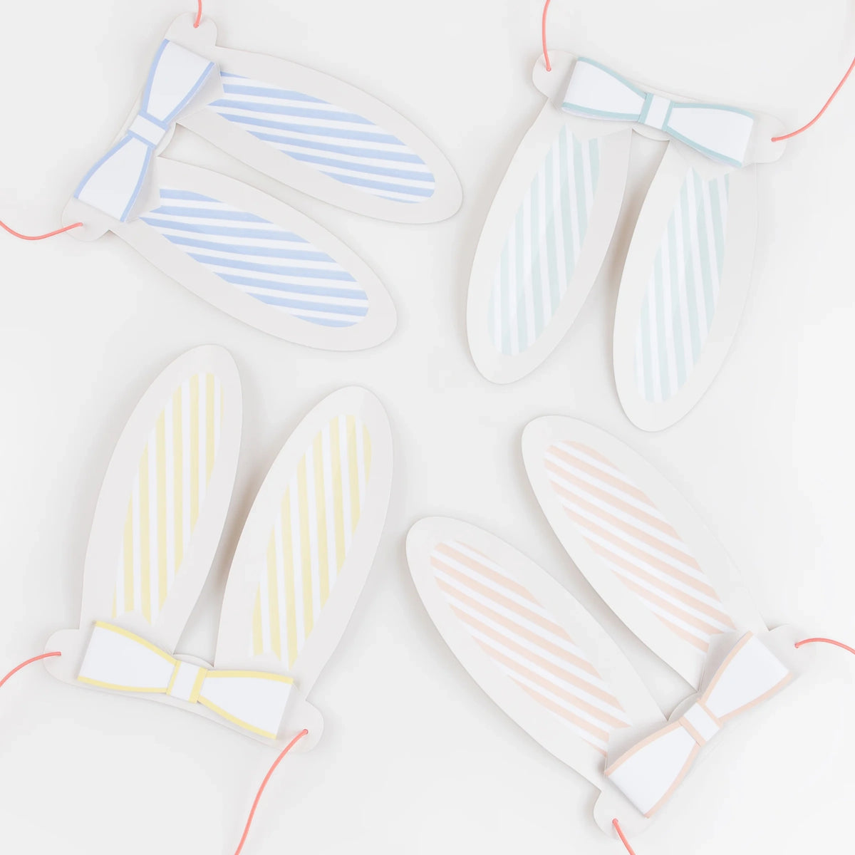 Four sets of pastel striped paper bunny ears with matching bow ties and pink elastic strings on a white background.