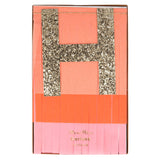 Meri Meri pink and peach fringed Happy Birthday garland set featuring a large gold glitter "H" in a gift box.