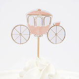 A pink and gold princess carriage cupcake topper with wheels, stuck into white frosting.