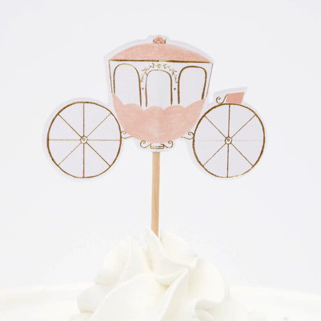 A pink and gold princess carriage cupcake topper with wheels, stuck into white frosting.