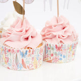Two frosted pink cupcakes in patterned floral liners with wooden picks, on a white background.