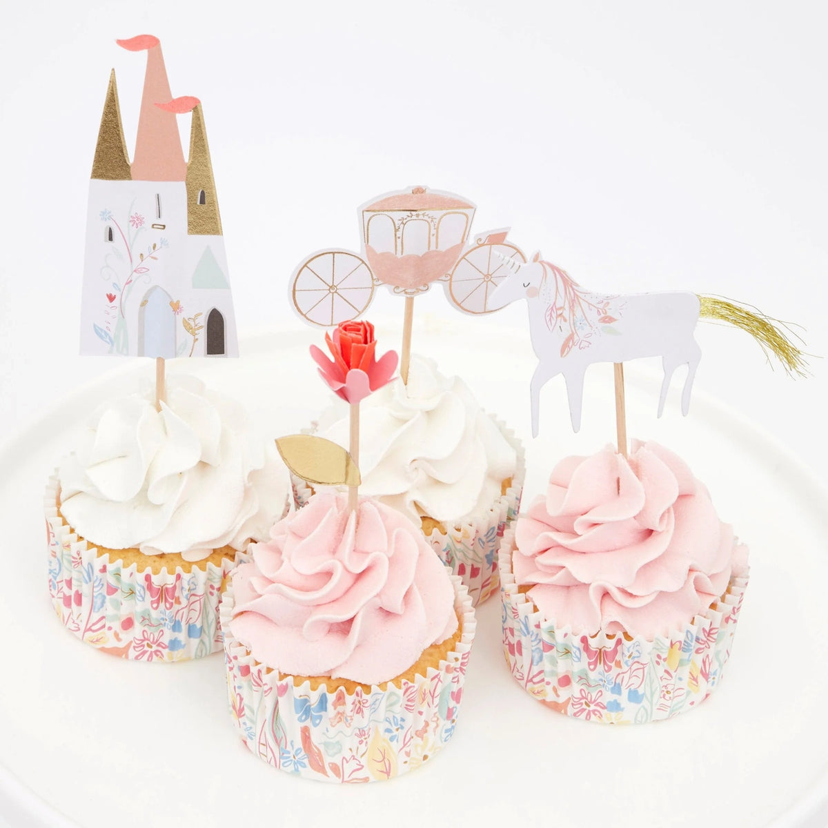 Four cupcakes with pink and white frosting featuring princess-themed toppers: a castle, carriage, rose, and unicorn.