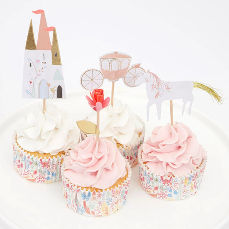 Four cupcakes with pink and white frosting featuring princess-themed toppers: a castle, carriage, rose, and unicorn.