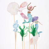Watercolor mermaid, seahorse, seashell, and seaweed cutouts on wooden sticks against a white background.