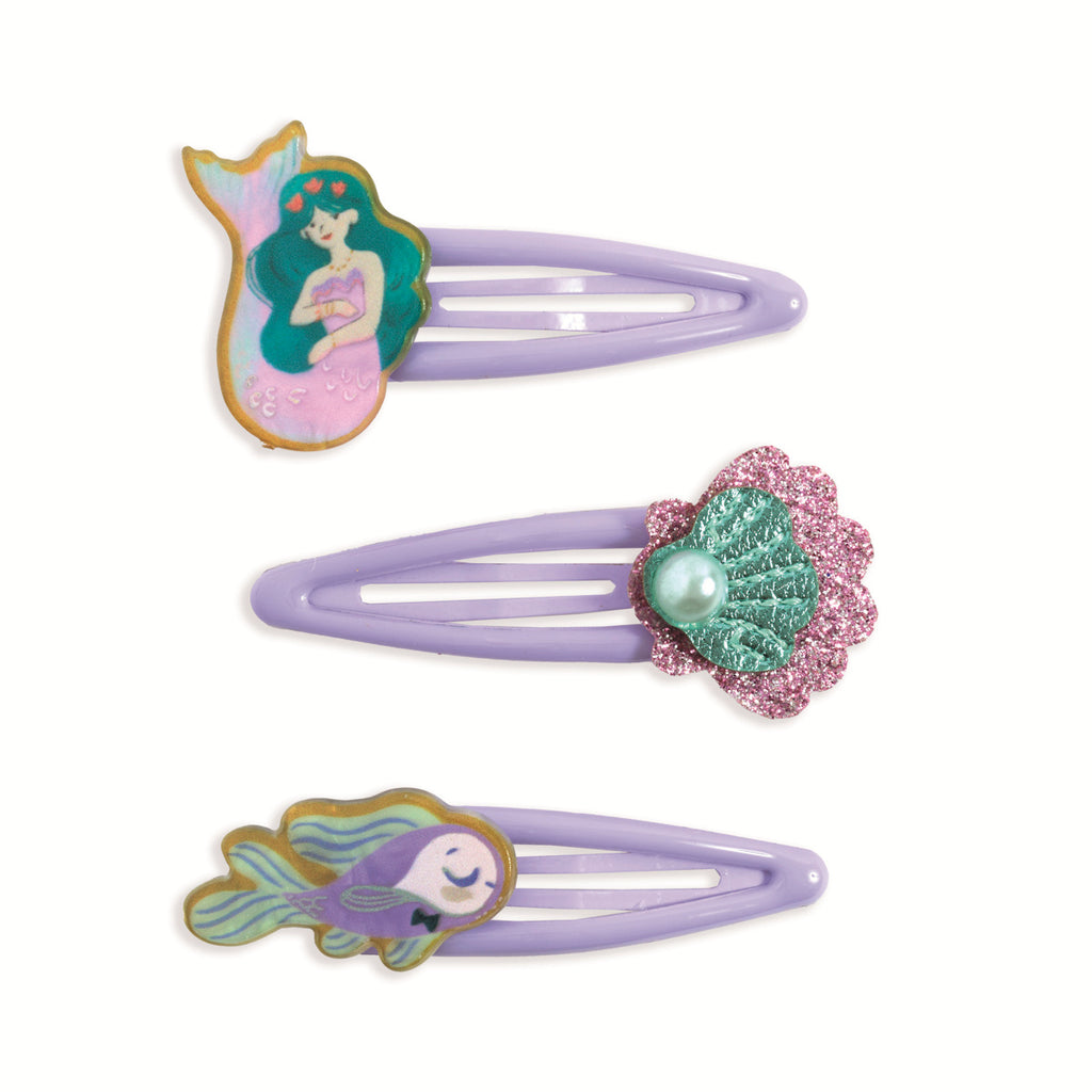 Three purple hair clips with ocean-themed designs, a mermaid, a glittery seashell with a pearl, and a smiling fish, conveying a whimsical, playful tone.