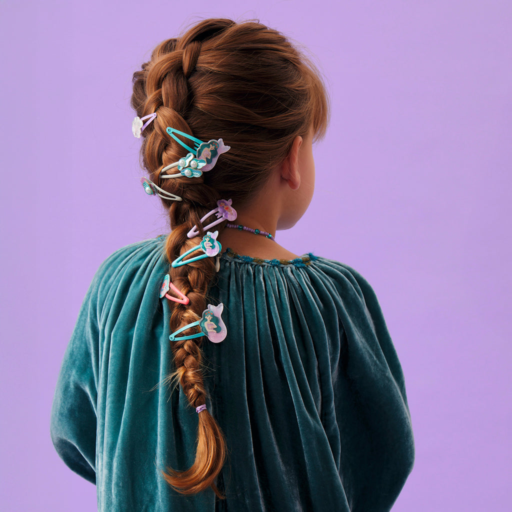 Braided hair adorned with colorful, whimsical hair clips featuring shapes like clouds and flowers, set against a soft purple background.