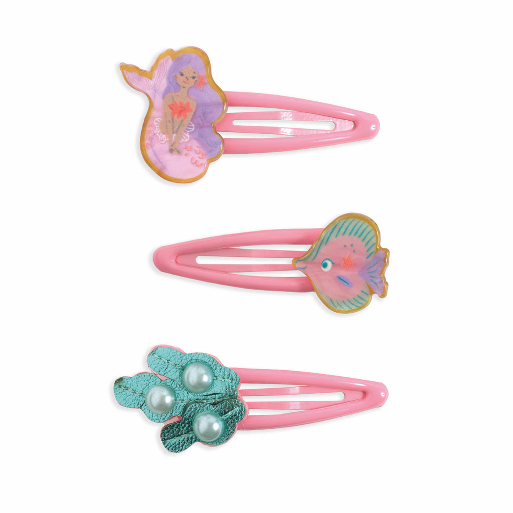 Three pink hair clips with colorful designs. Top clip has a mermaid motif, middle features a fish, and bottom showcases teal leaves with pearls. Playful tone.