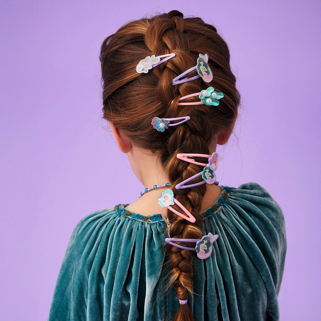 Braided hair adorned with colorful, whimsical hair clips featuring shapes like clouds and flowers, set against a soft purple background.
