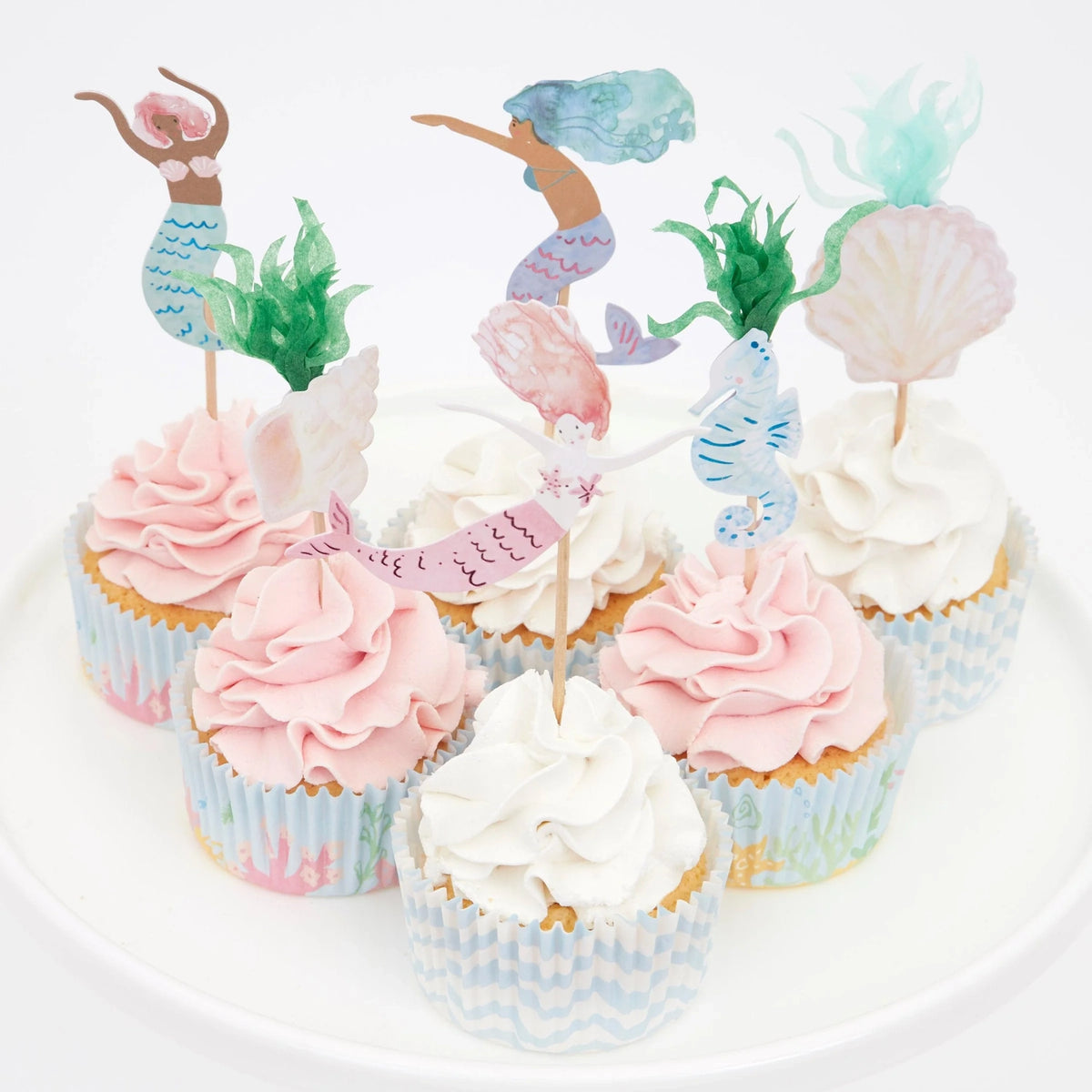 Six cupcakes with pink and white frosting, decorated with mermaid, seahorse, and seashell toppers.