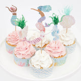 Six cupcakes with pink and white frosting, decorated with mermaid, seahorse, and seashell toppers.
