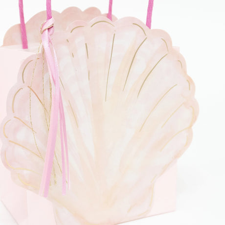 Pink seashell-shaped gift bag with gold accents and ribbon handles.