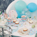 A mermaid-themed party setup with cupcakes, fringed cups, and blue balloons by a bathtub.