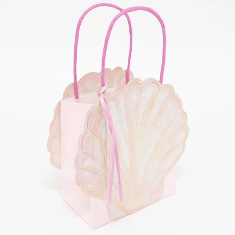 Pink seashell-shaped gift bag with bright pink handles and a small ribbon tassel against a white background.