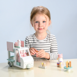 Young girl playing with a wooden toy milkshake van and cat figures at a table.