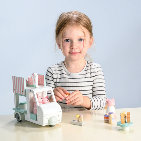 Young girl playing with a wooden toy milkshake van and cat figures at a table.