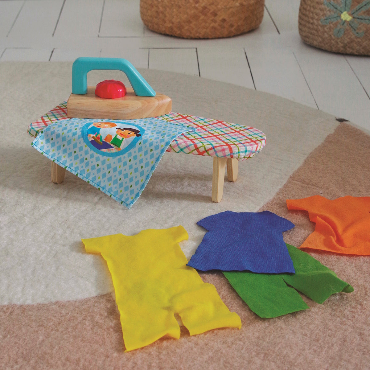 Wooden toy iron and ironing board set with colorful felt doll clothes on a play room rug.