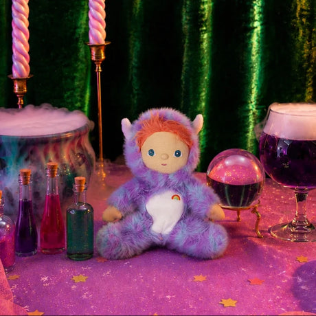 Plush doll in a fuzzy purple monster suit on a mystical table with potion bottles and crystal ball.