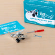 A construction set with a partially assembled toy plane is on a table. Nearby are a blue instruction manual, a red screwdriver, and a small wrench.