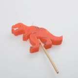 Close-up view of an orange T-Rex dinosaur birthday candle on a wooden pick.
