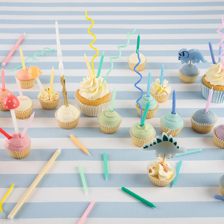 Flat lay of frosted cupcakes with birthday candles and dinosaur picks on blue striped paper.
